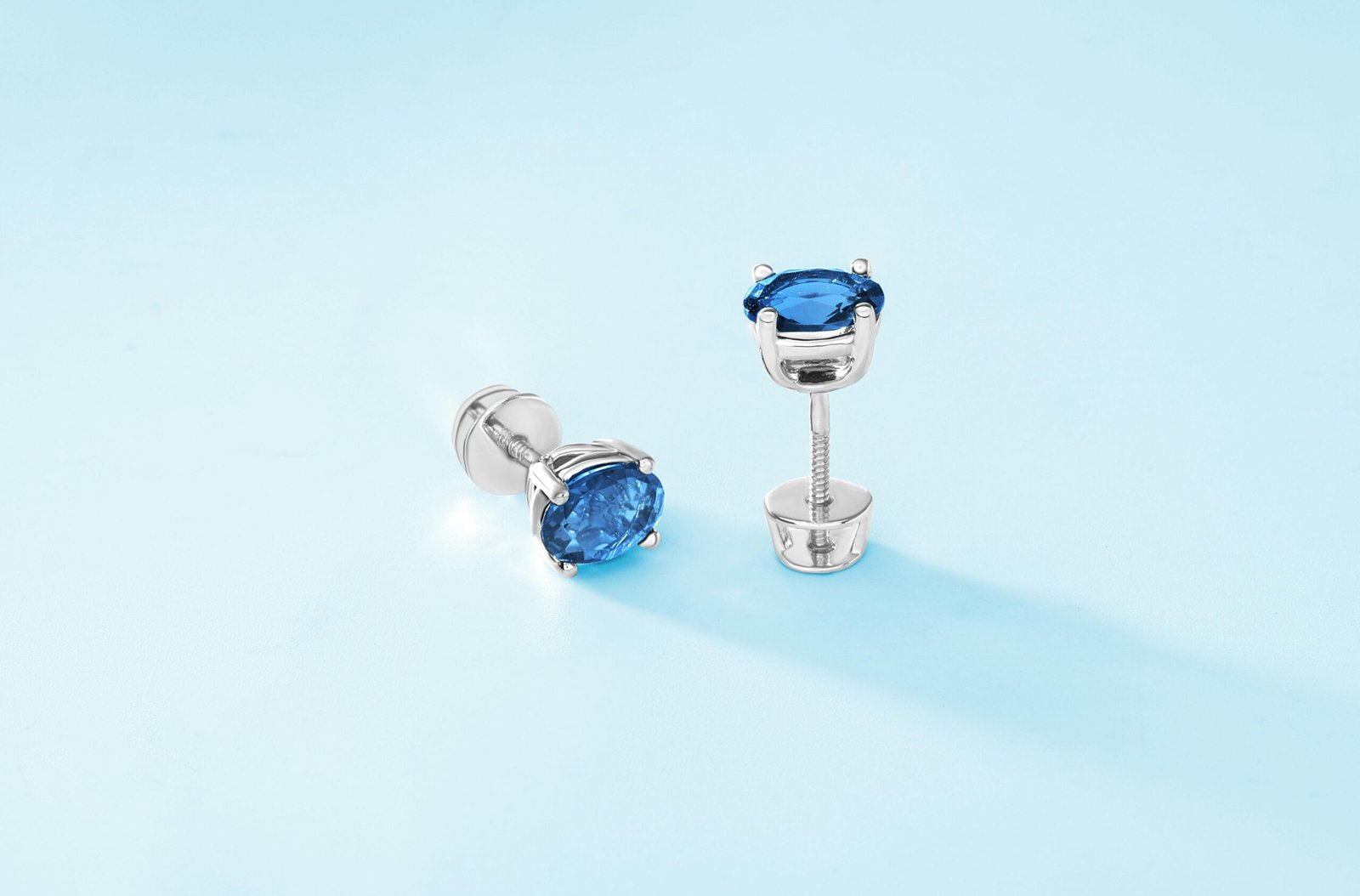 Luxurious silver stud earrings with blue gemstones on a soft blue background.